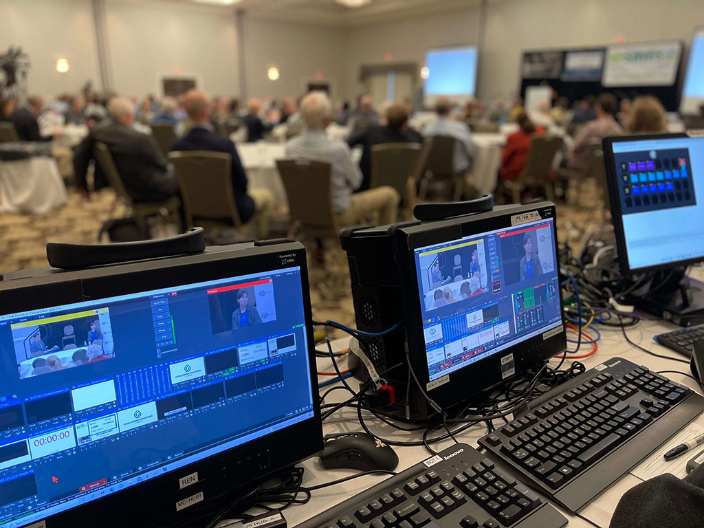 monitors and keyboard and other event production equipment shot with the conference audience in front