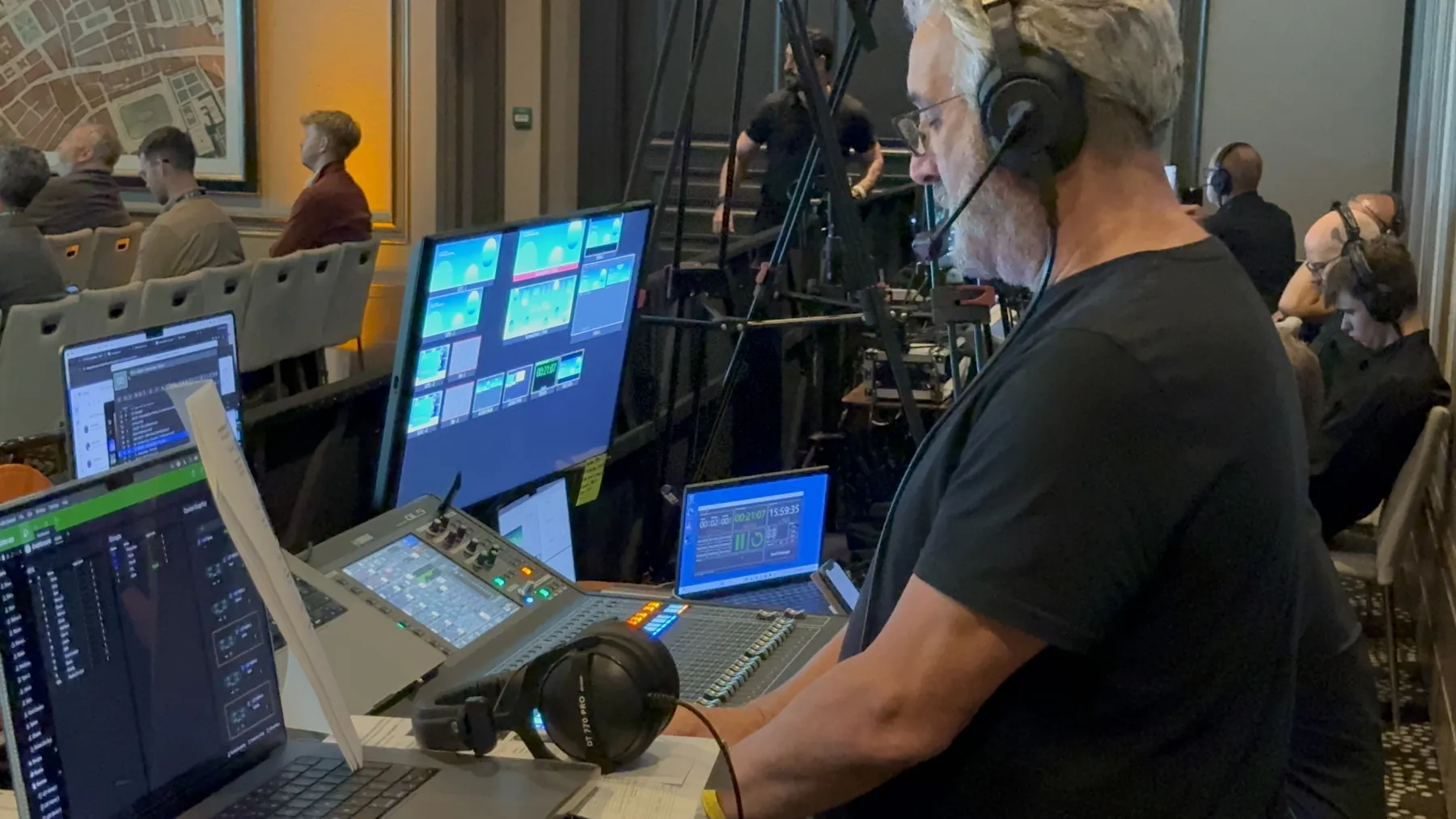A crew member on headset at the show desk with monitors and a laptop, the audience seated beyond.