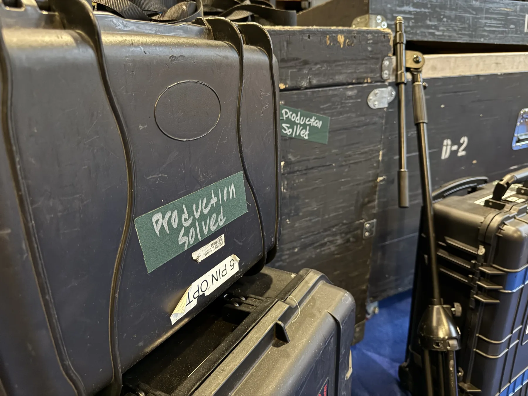 Road cases hand-labeled "Production Solved" stacked backstage, packed for the next city.