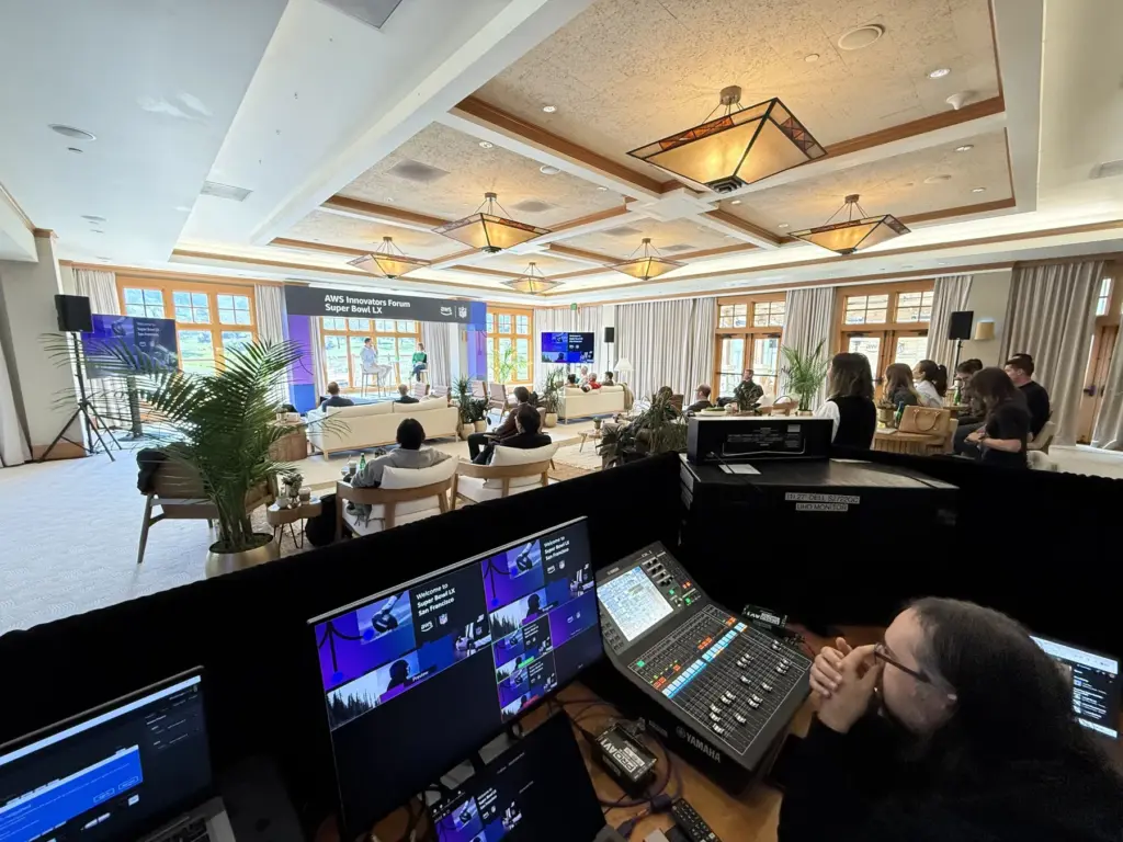 A producer at the show desk in a hotel ballroom, with multiview monitors and an audio console in front of the room.