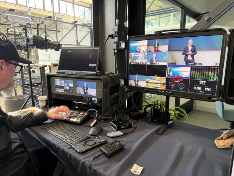 A compact control position with a switcher and monitors showing a live program feed.