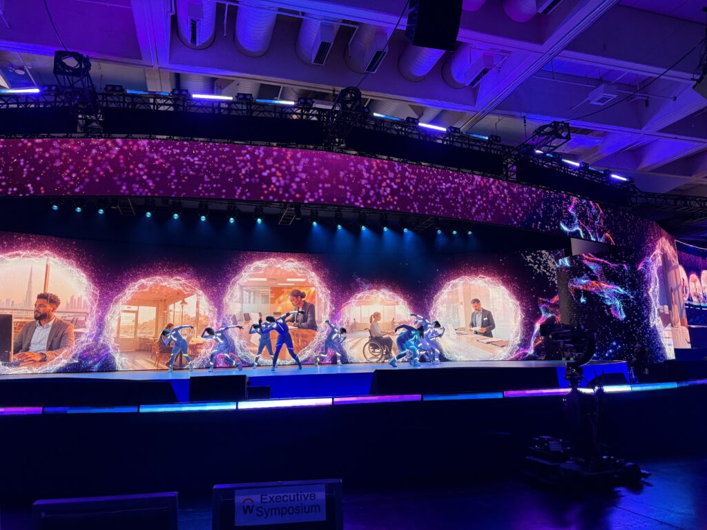 A keynote opener on a large stage with glowing circular set pieces and performers, under purple and blue light.