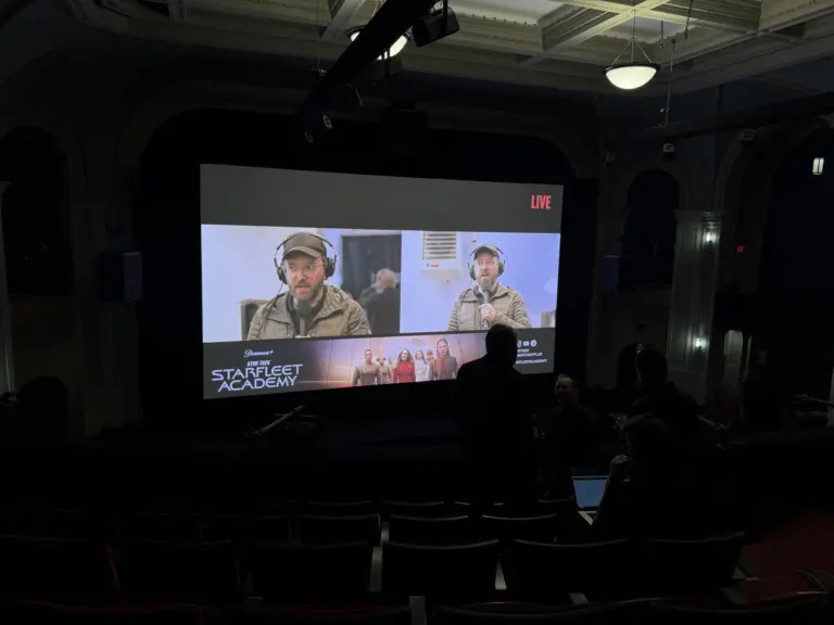 Two remote guests appear live in split screen on a theater's big screen during a screening event.