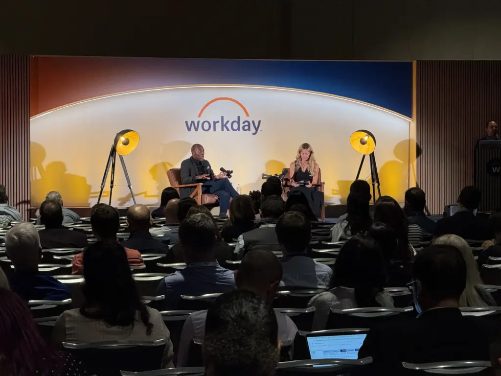 A fireside chat on a Workday stage with two yellow lamps, seen past a seated audience.