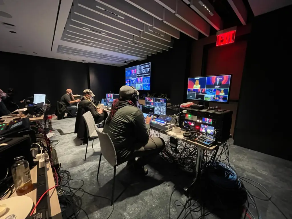 Crew on headset in a control room during a global town hall broadcast from London and New York, with multiviewers and the live program on screen.