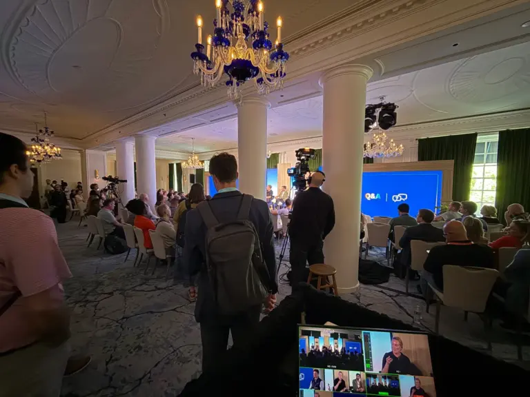 A conference panel in a hotel ballroom seen from the production position, with a camera operator on headset, a Q&A slide on the LED wall and the live switcher multiview in the foreground.