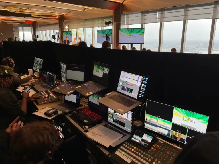 Our production position at a financial conference high above the Hudson: switcher, graphics and playback stations behind pipe and drape, with a panel on stage beyond.